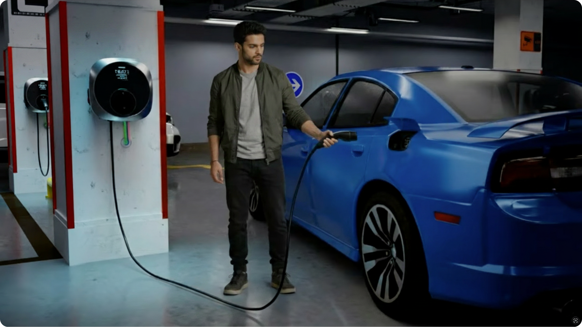 A man charging a blue EV in a basement parking area using a wall-mounted Motron charger