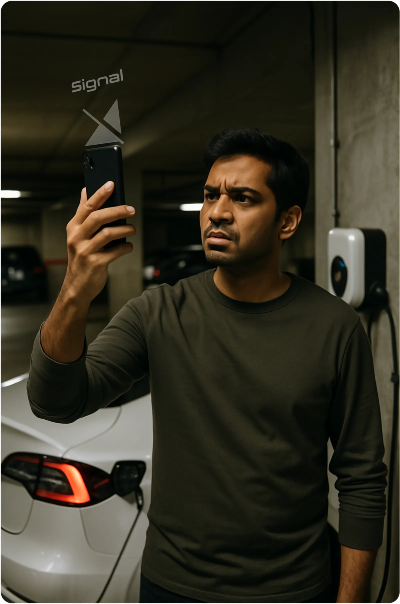 A man in a dim basement holding up his phone searching for a signal beside an EV charger